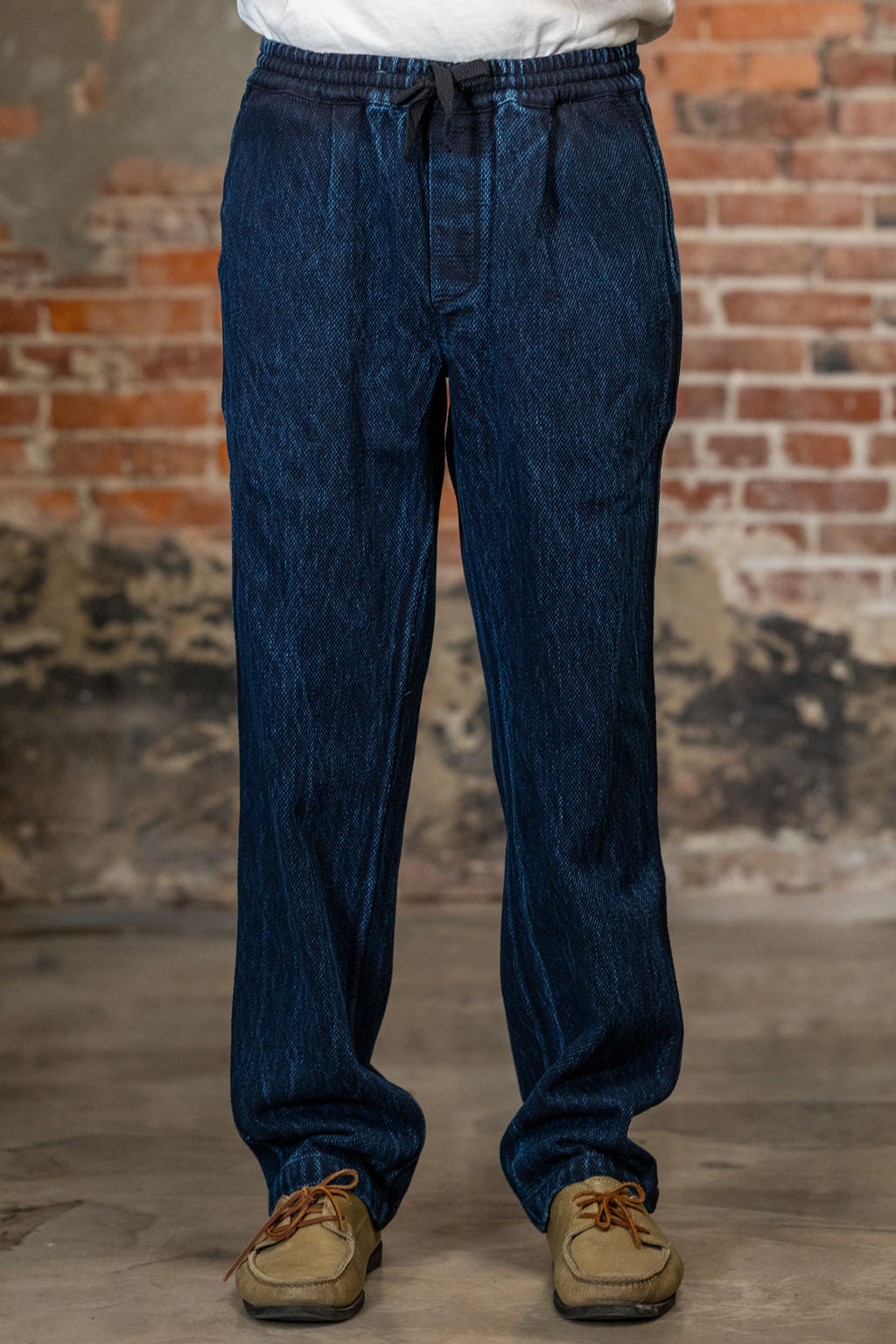 A person wearing the 3sixteen Easy Pant - Indigo Kendo Cloth n front of a rustic brick wall.