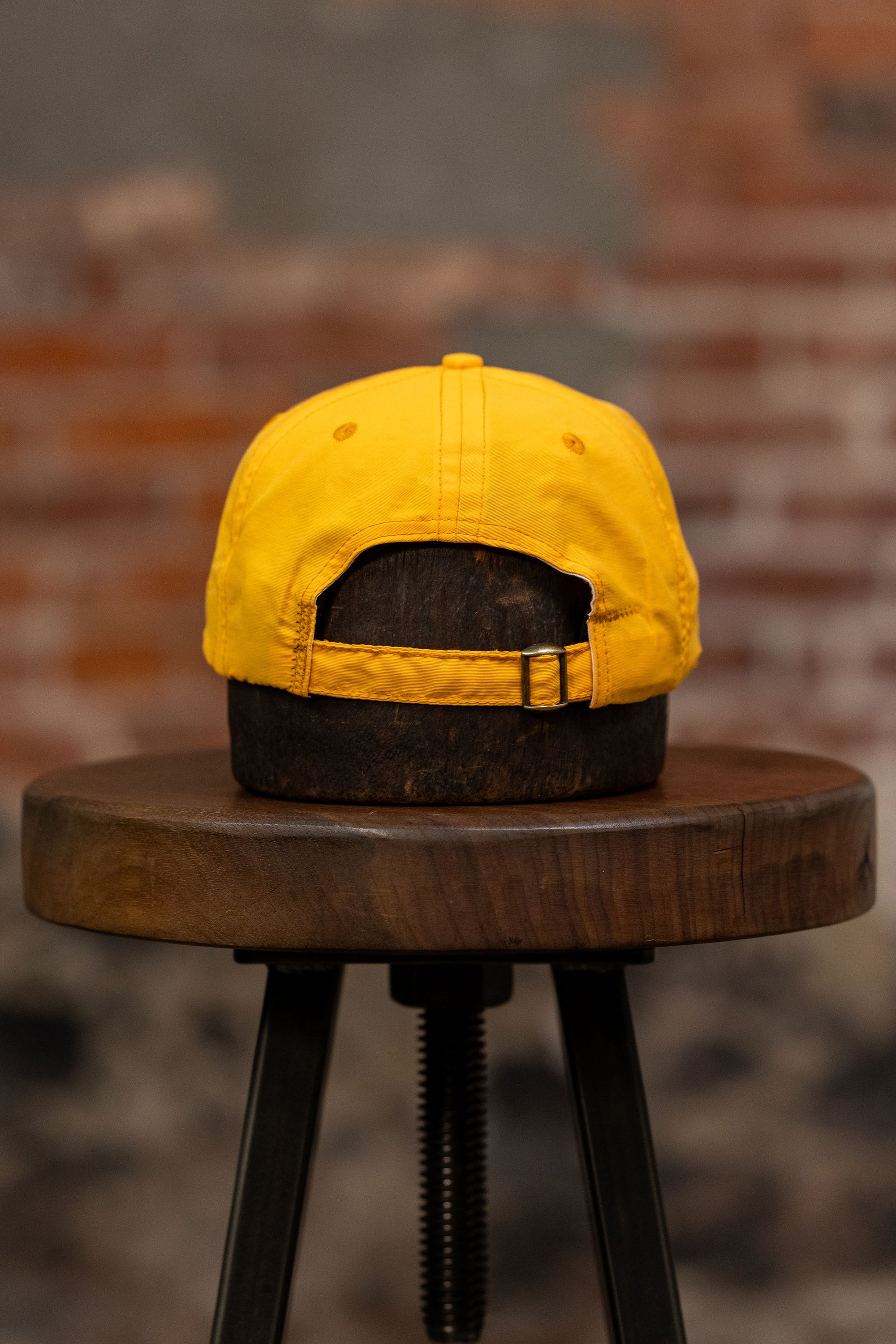 Franklin & Poe Surf Cap - Nylon Gold on stool, facing away from the camera. Showing adjustable strap. 

