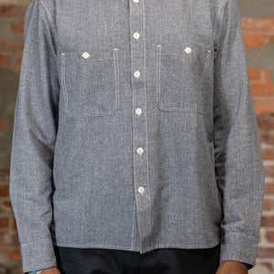A person shown from the front wearing the 3sixteen Utility Chambray Shirt - Handloom Silk Khadi, while standing in front of a rustic brick wall.