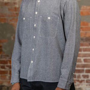 A person shown from the side wearing the 3sixteen Utility Chambray Shirt - Handloom Silk Khadi, while standing in front of a rustic brick wall.