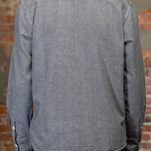 A person shown from the back wearing the 3sixteen Utility Chambray Shirt - Handloom Silk Khadi, while standing in front of a rustic brick wall.