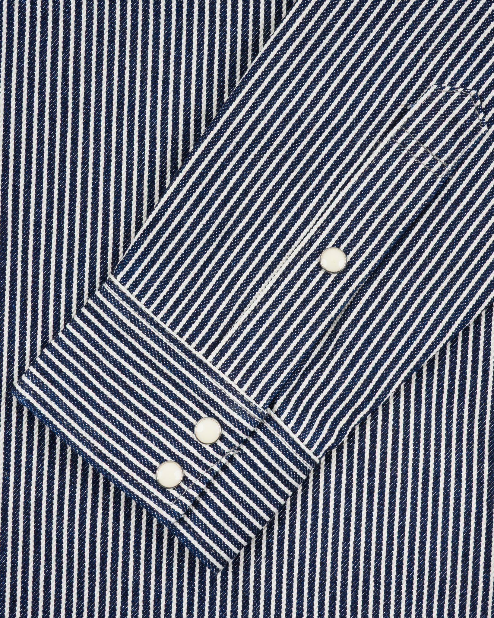Western style shirt with indigo and white thin vertical stripes and white snaps close-up on sleeve buttoned