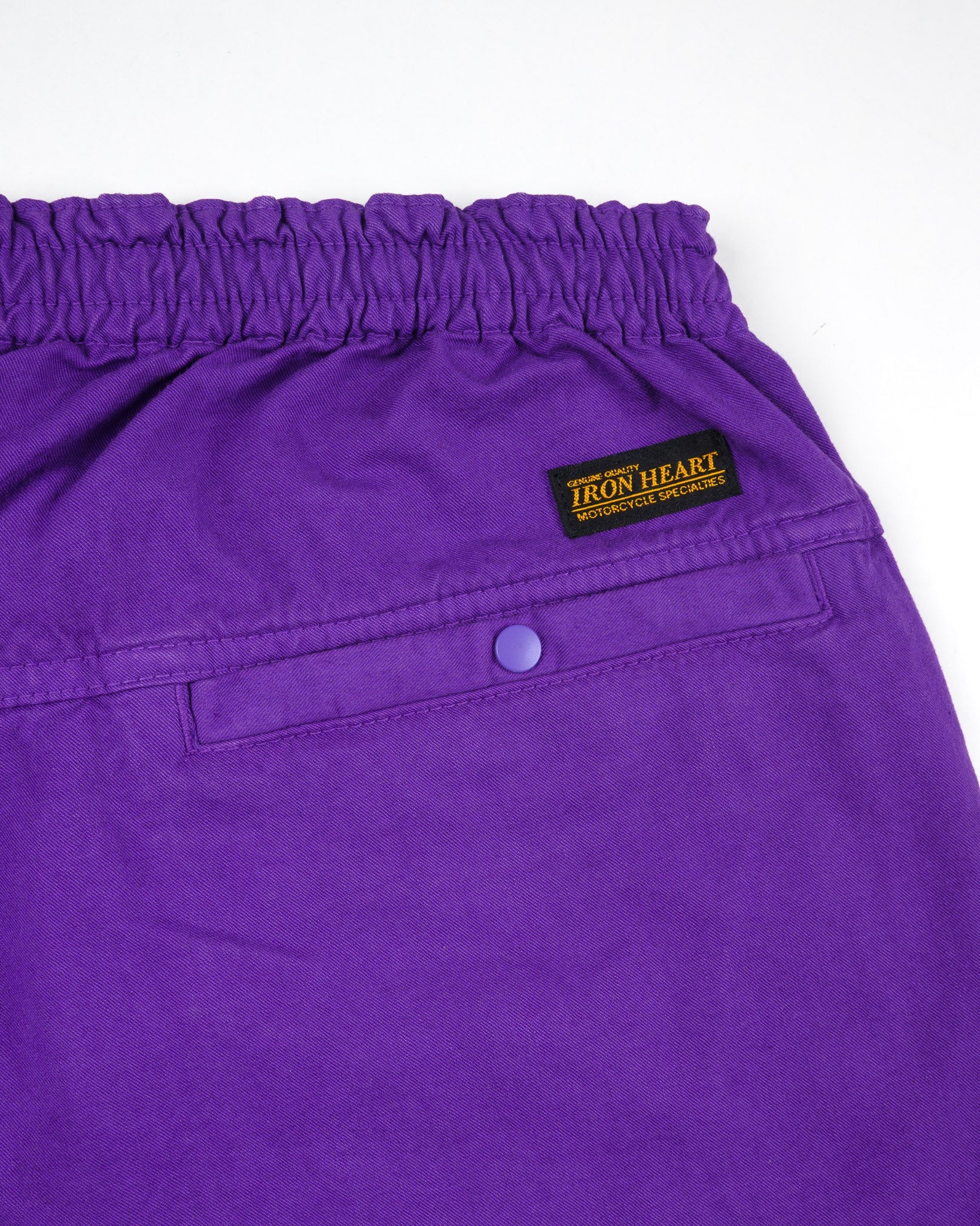 Purple mid length shorts back view laying flat closeup on snap pocket and black/yellow Iron Heart logo