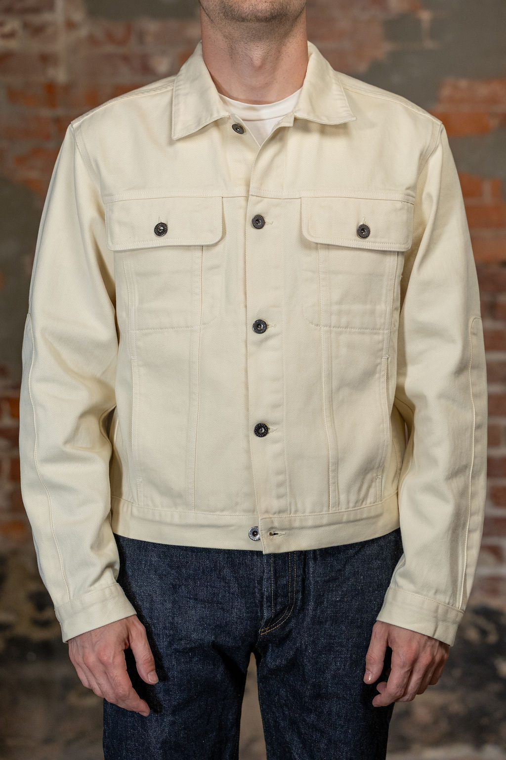 A person viewed from the front is wearing the  3sixteen Trucker Jacket - Buttermilk Twill which is a light cream canvas utility jacket 