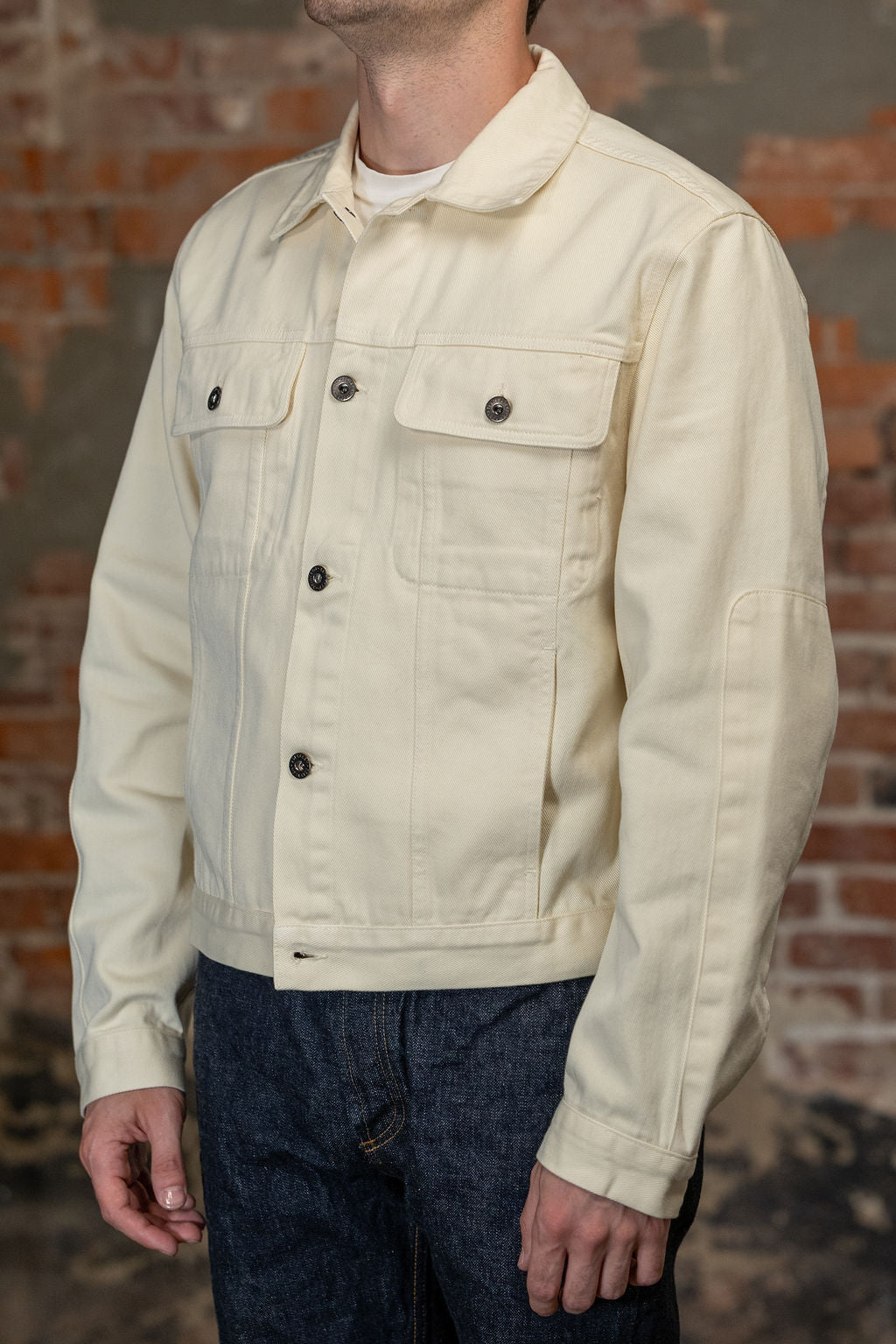 A person viewed from the side wearing the  3sixteen Trucker Jacket - Buttermilk Twill which is a light cream canvas utility jacket