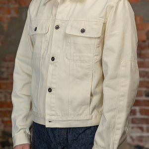 A person viewed from the side wearing the  3sixteen Trucker Jacket - Buttermilk Twill which is a light cream canvas utility jacket