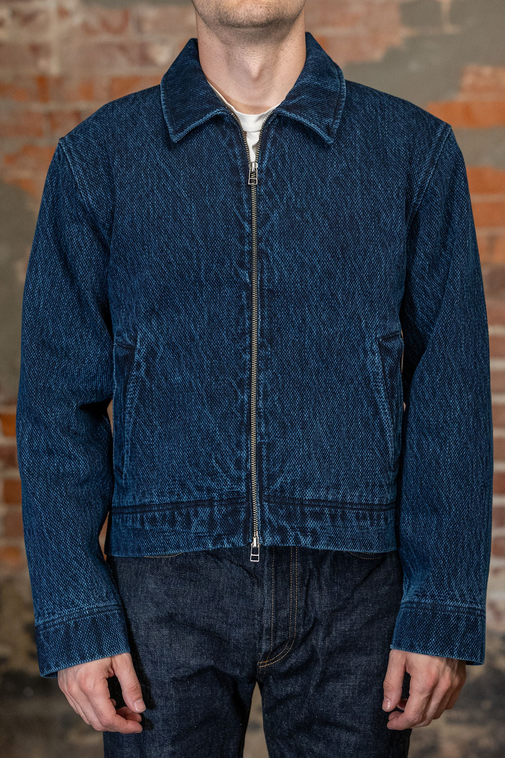 Front view of  person wearing 
the 3sixteen Club Jacket - Indigo Kendo Cloth, standing against a rustic brick wall.
