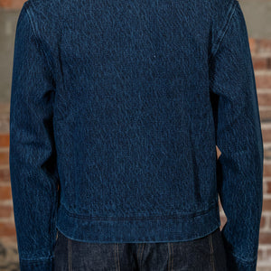 A person viewed from the back wearing 
the 3sixteen Club Jacket - Indigo Kendo Cloth, standing against a rustic brick wall.