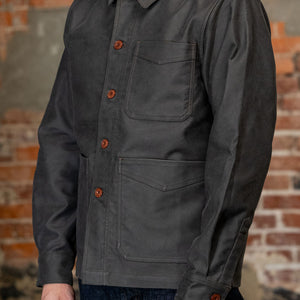 A man viewed from the side wearing
3sixteen French Work Jacket - Grey Moleskin, a dark charcoal gray long-sleeve button-up shirt 