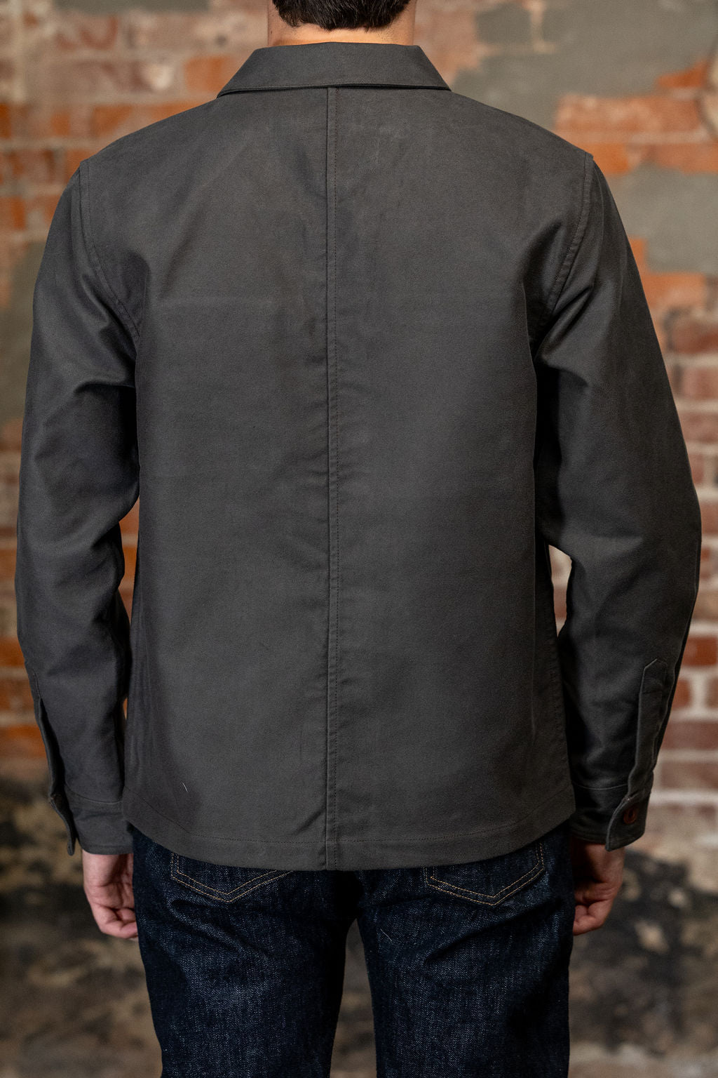 A man viewed from the back wearing
3sixteen French Work Jacket - Grey Moleskin, a dark charcoal gray long-sleeve button-up shirt 