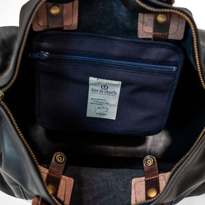 Black duffel bag with brown handles closeup on navy internal lining and pocket with white label
