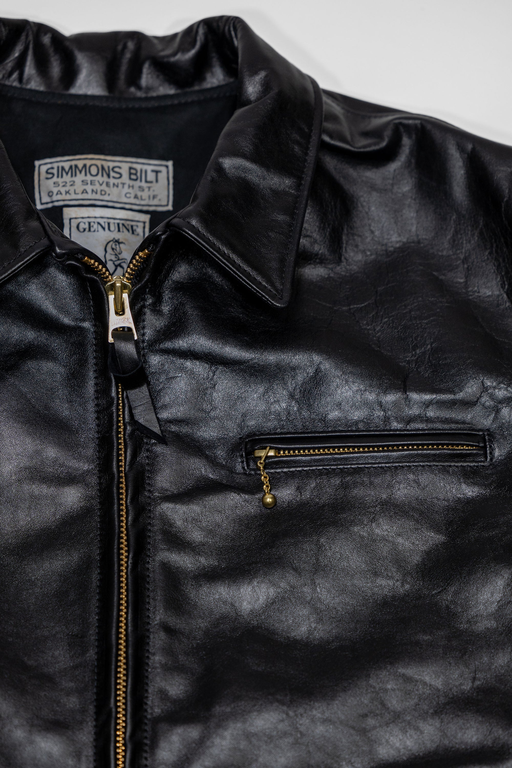 Black leather jacket laid flat on white. details of chest zipper & collar. 