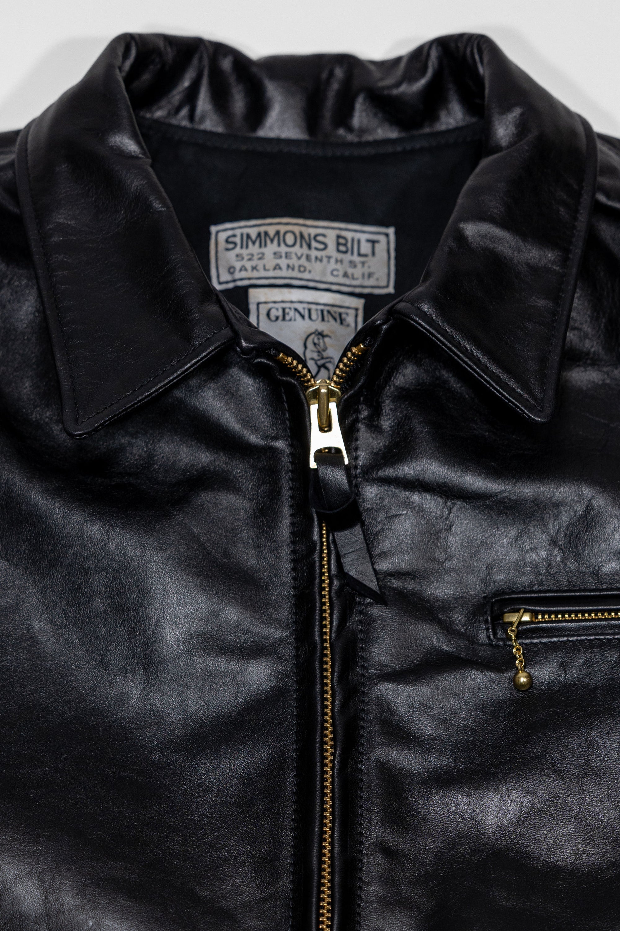 Black leather jacket laid flat on white. Detail of collar & zipper