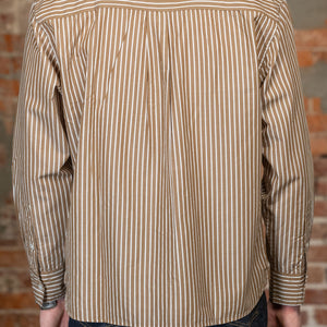 A man viewed from the back wearing the 
3sixteen Commuter Shirt - Brown Ecru Stripe, a beige and brown vertically striped long-sleeve button-down shirt and dark blue jeans, standing against a rustic brick wall.