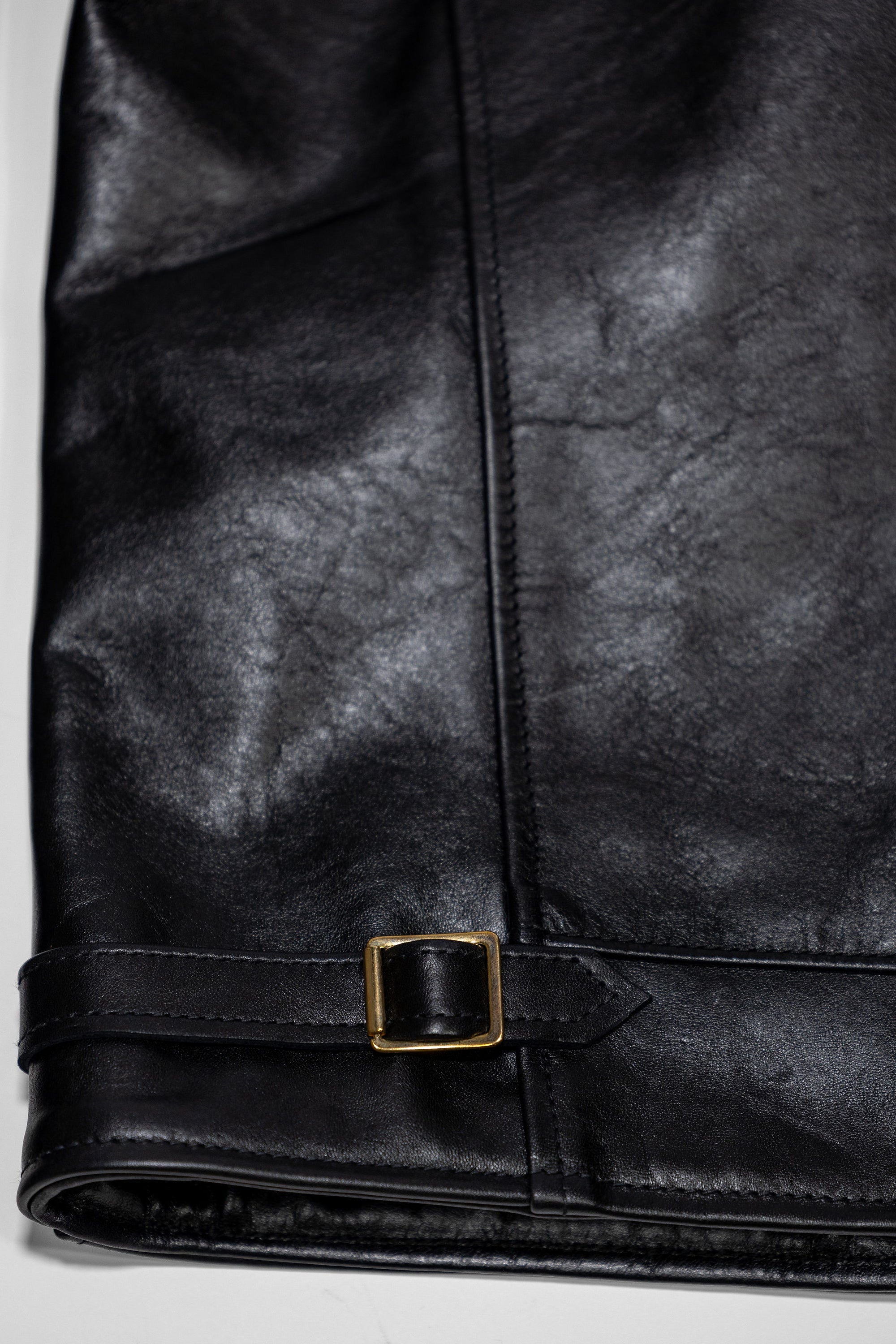 Black leather jacket laid flat on white. Details of side cinch.  