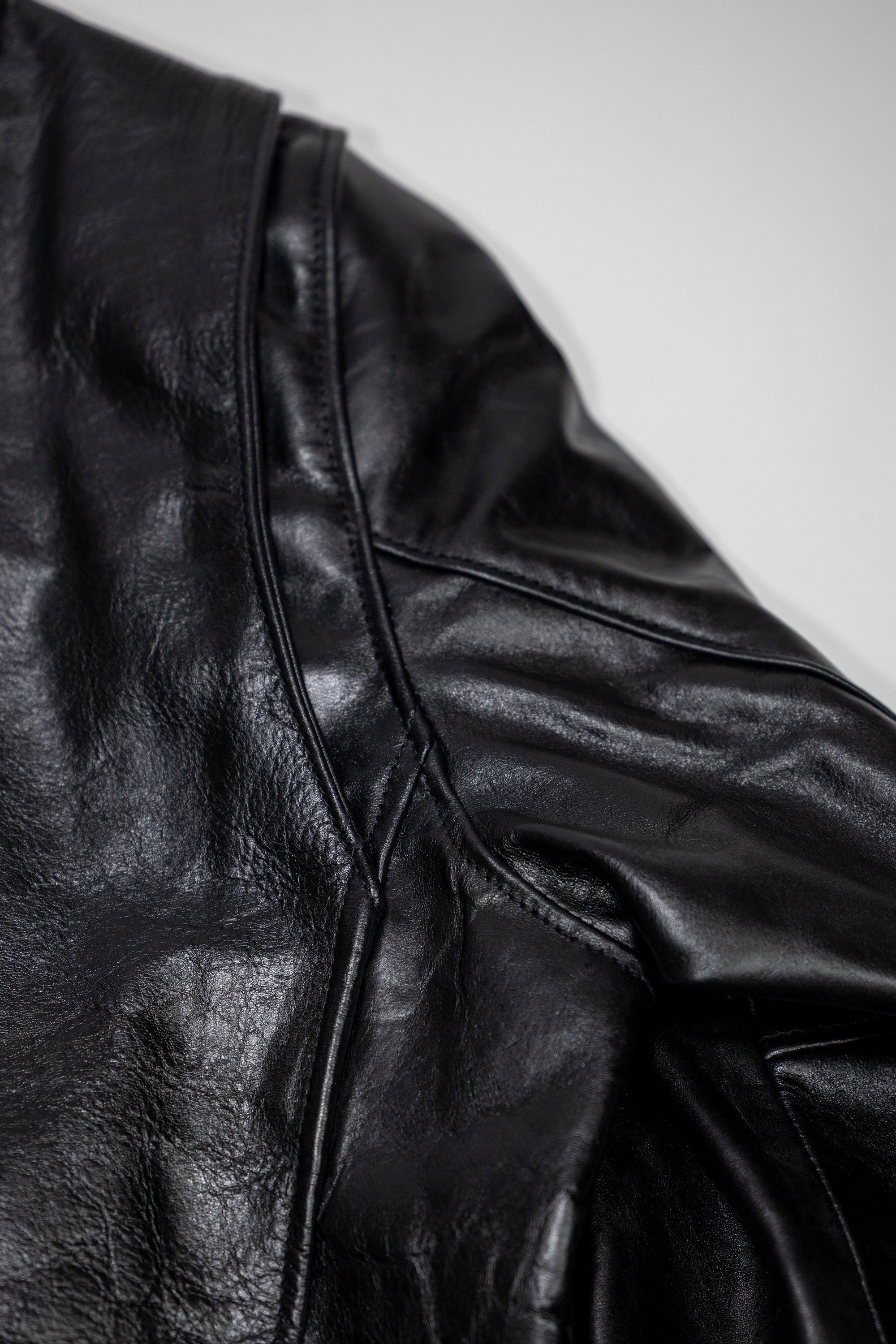 Black leather jacket laid flat on white. Details of sleeve gusset. 