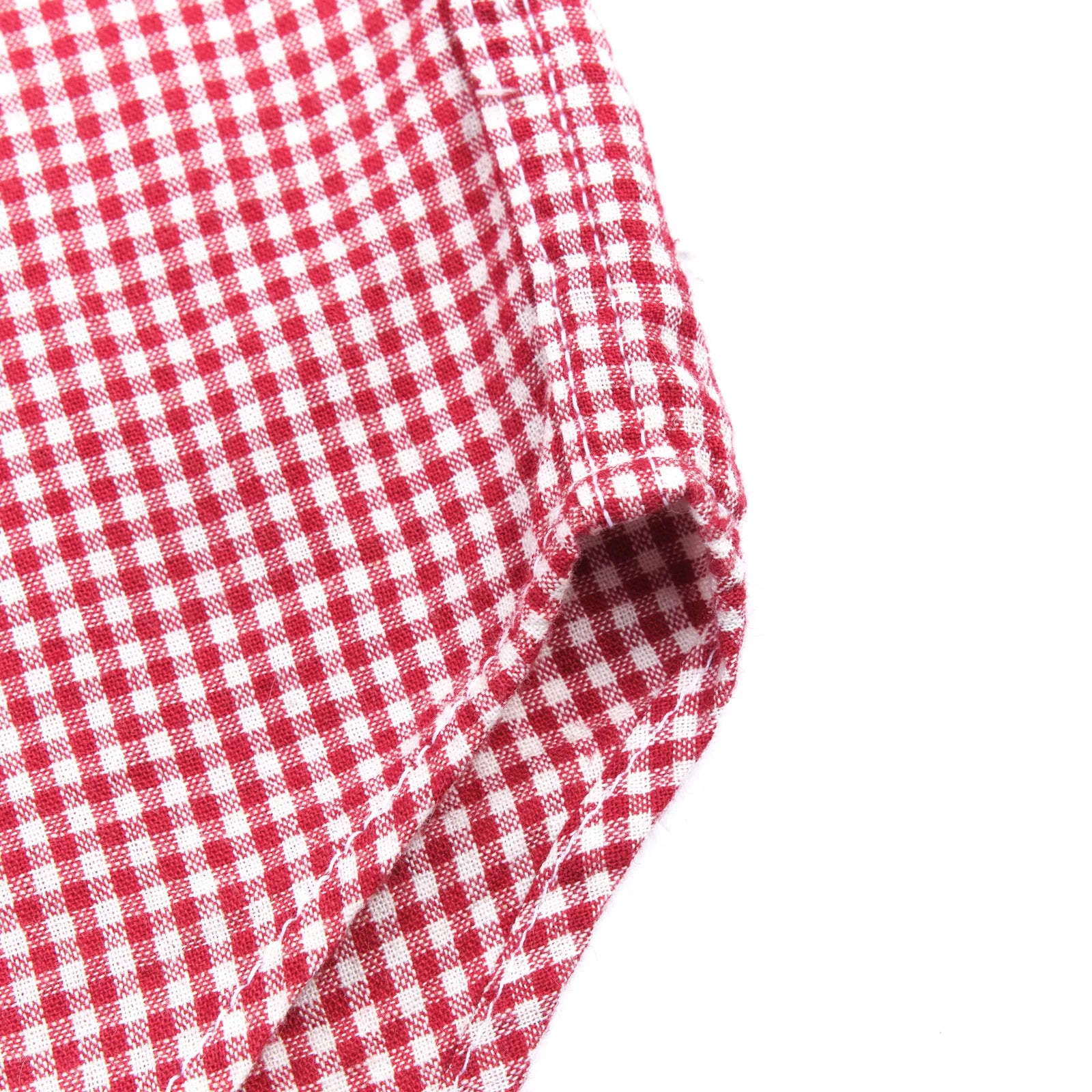 Red and white gingham western-style button-down shirt close up on hem and side seam laying flat