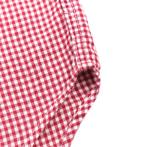Red and white gingham western-style button-down shirt close up on hem and side seam laying flat