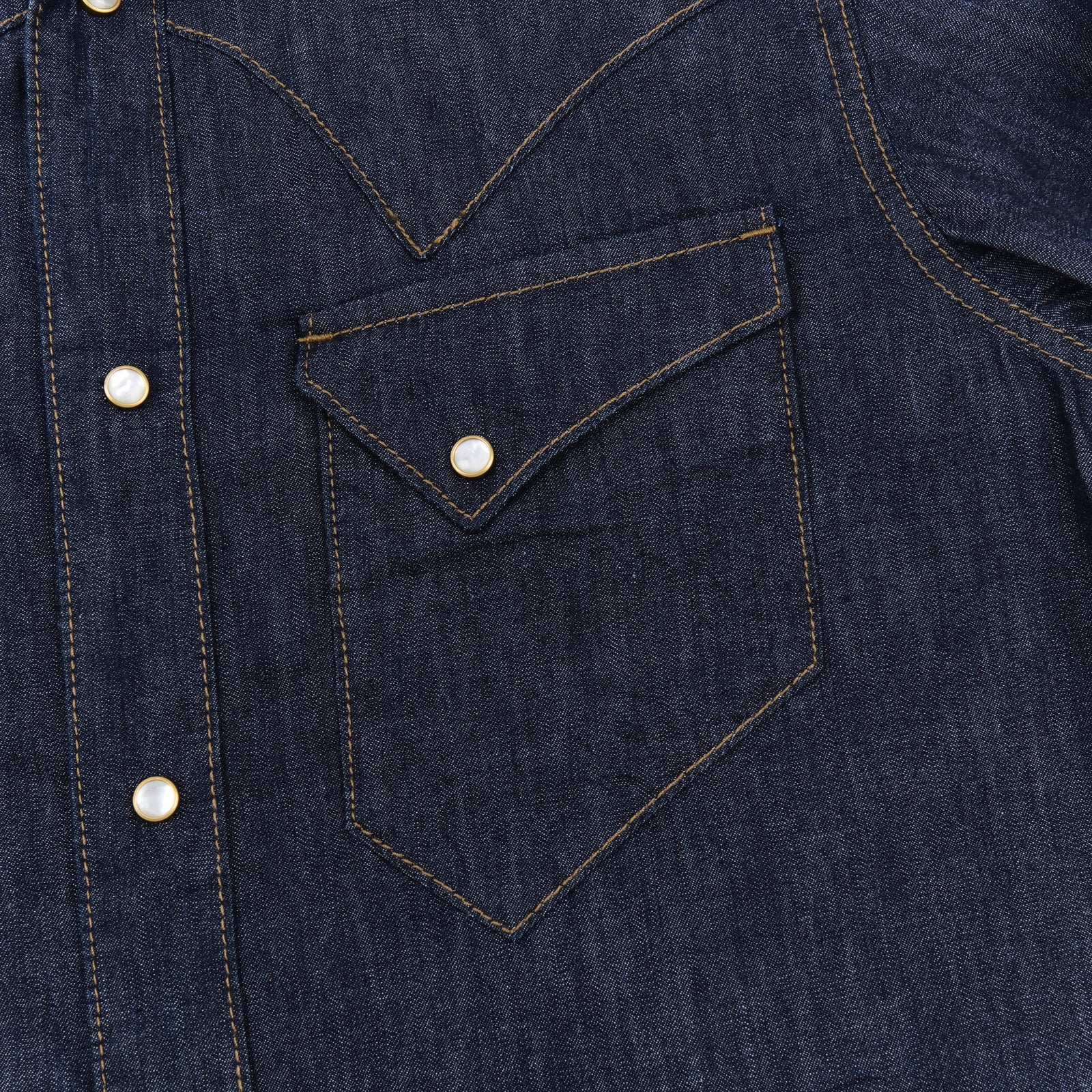 Dark indigo denim western-style shirt with white snaps, close up on left chest pocket laying flat