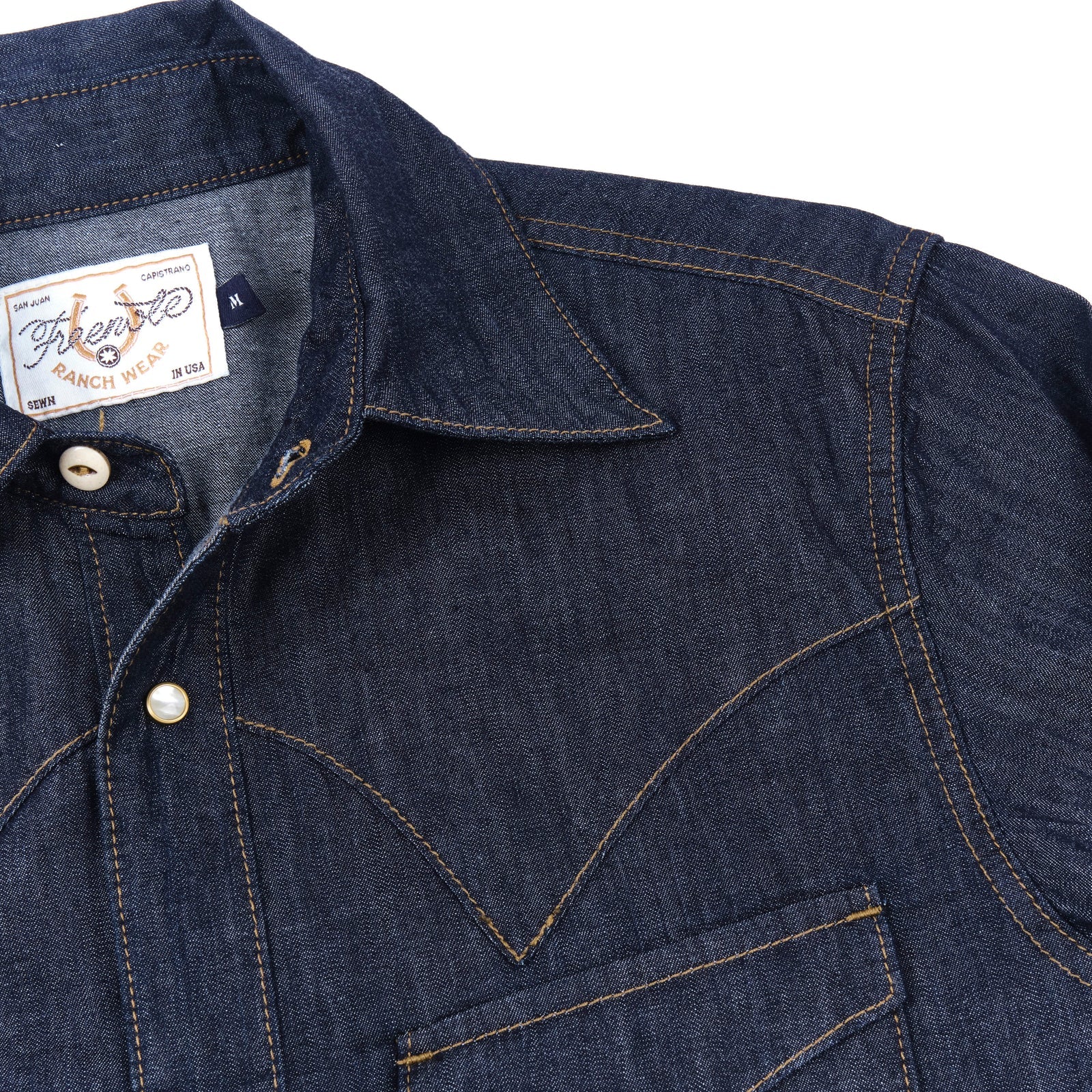 Dark indigo denim western-style shirt with white snaps, close up on shoulder laying flat